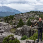 Wandelaar met stokken op een plateau van afgesleten kalkrotsen met jeneverbessen, met de bewolkte bergen van het Taurusgebergte erachter