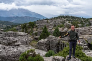 Wandelaar met stokken op een plateau van afgesleten kalkrotsen met jeneverbessen, met de bewolkte bergen van het Taurusgebergte erachter