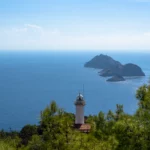 Witte vuurtoren van Gelidonya tussen de dennen, met de eilanden voor Kaap Gelidonya in de Middellandse Zee, Lycian Way bij Adrasan, Turkije