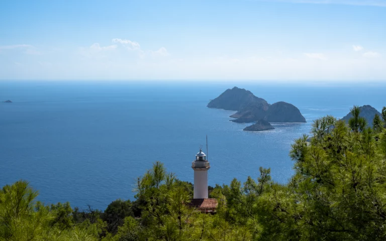 Witte vuurtoren van Gelidonya tussen de dennen, met de eilanden voor Kaap Gelidonya in de Middellandse Zee, Lycian Way bij Adrasan, Turkije