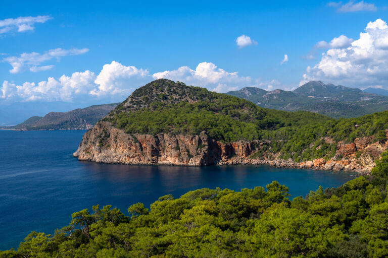 Rode kalksteenkliffen en beboste heuvels aan een diepblauwe baai op de Lycian Way bij Adrasan, Turkije